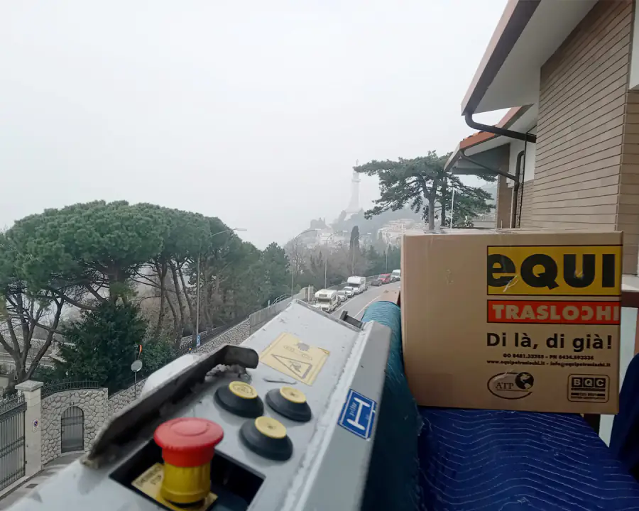 Trasloco a Trieste con l'elevatore: lo scatolone Equipe arriva al balcone e sullo sfondo, nella nebbia, il Faro della Vittoria